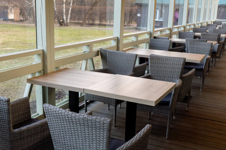 Outdoor cafe seating with modern wicker chairs and wooden tables on a terraceの写真素材