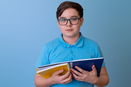 Young caucasian male teen holding notebooks in blue shirt on light blue backgroundの写真素材