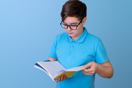 Caucasian young male teen reading notebook in blue shirt against blue backgroundの写真素材