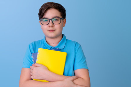Caucasian male teen holding notebooks against blue background with confident expressionの写真素材