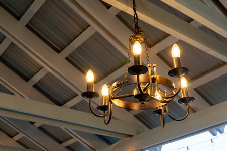 Rustic vintage chandelier hanging from wooden beamed ceiling illuminated with warm bulbsの写真素材