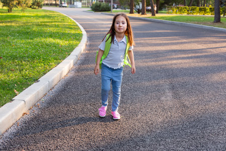 Young girl walking on park path with backpack on sunny dayの写真素材