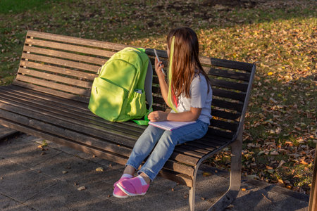 Young girl on park bench with backpack and smartphone in autumn settingの写真素材
