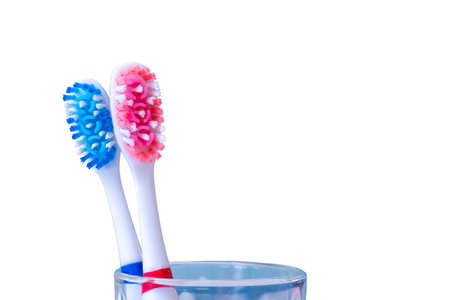 Two colorful toothbrushes in glass cup on white backgroundの写真素材