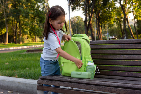 Young girl packing green backpack on park benchの写真素材