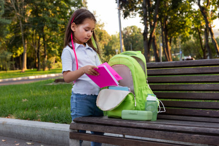 Young girl organizing backpack on park bench in sunny weatherの写真素材