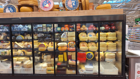 Russia, Moscow- 21 October 2025.Glass display case filled with a diverse assortment of cheeses in a grocery storeのeditorial素材