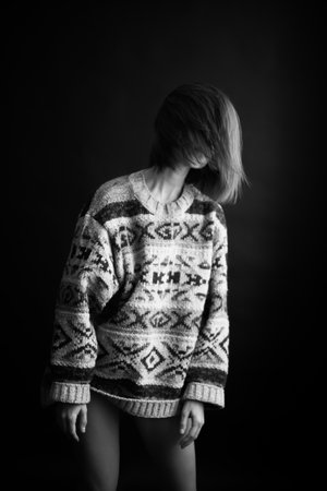 brunette girl in a cozy sweater with an ethnic ornament poses freely on a black backgroundの写真素材