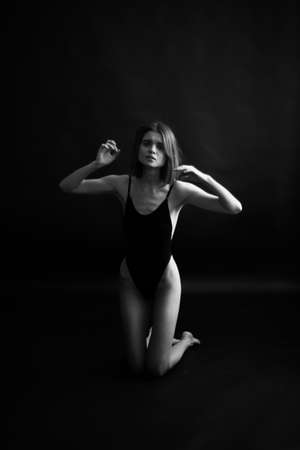 brunette in a black bodysuit sits on the floor and moves randomly, posing as a dancer and improvising body plasticsの写真素材