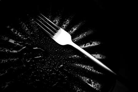 an empty black plate and a fork on it, wet dishes, beautiful raindrops on the terrace in a cafeの写真素材