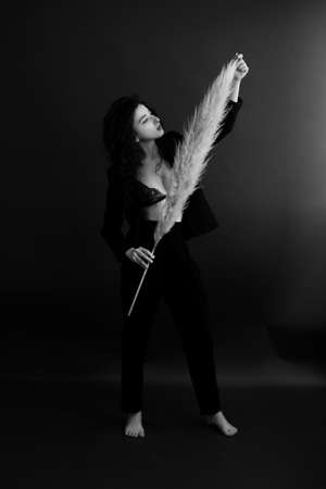 fashion studio portrait of girl in dark clothes with large dried flower featherの写真素材