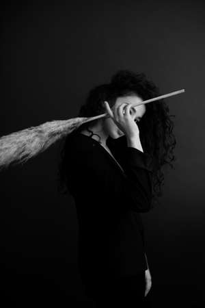 fashion studio portrait of girl in dark clothes with large dried flower featherの写真素材