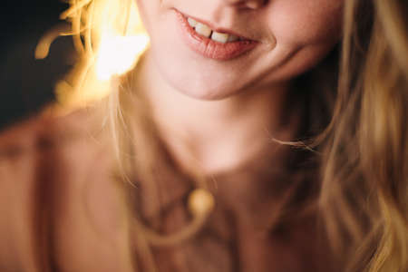 A beautiful girl in a brown blouse smiles cheerfully at the camera and plays with her wavy hair, a portrait of a young actress. soft focus backgroundの写真素材