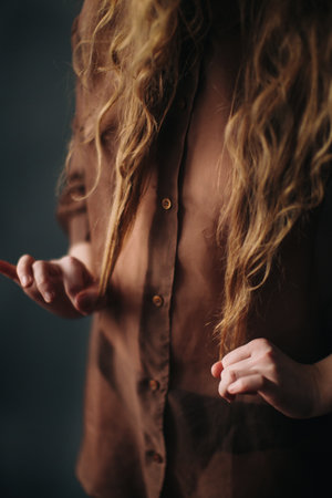 A beautiful girl in a brown blouse smiles cheerfully at the camera and plays with her wavy hair, a portrait of a young actress. soft focus backgroundの写真素材