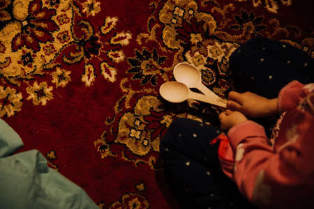A little girl plays with a wooden spoon on the carpet. Selective focus.の写真素材