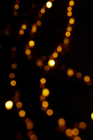 Defocused golden bokeh lights on black background. Christmas background.の写真素材