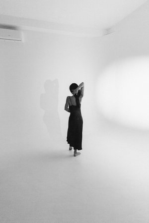 Woman in black dress walking in white room with shadow on wall.の写真素材