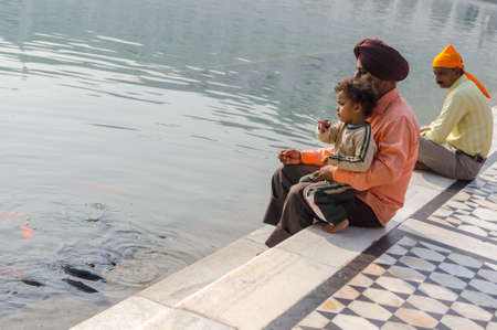 Amritsar, India - November 21, 2011: A Sikh family of pilgrims, father and son, are sitting near a lake in the Golden Temple complex. Amritsar, Punjab, India.のeditorial素材