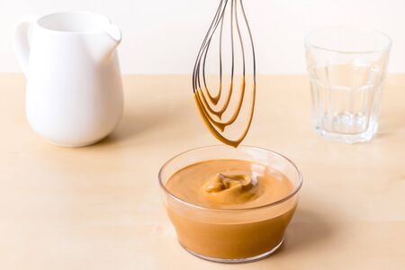 How to make coffee from dalgon. Step by step photo instruction. Step 4. Beat the cream. Ingredients - instant coffee, sugar, water, milk and a whisk for whipping on a wooden background.の写真素材