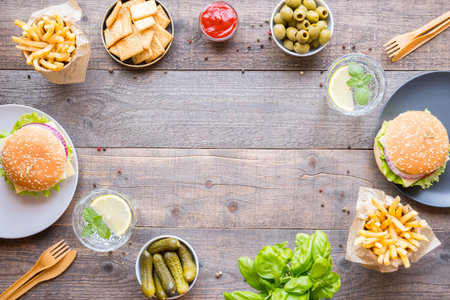 Dinner table with burger, french fries, vegetables, sauces, snacks and lemonade on wooden...