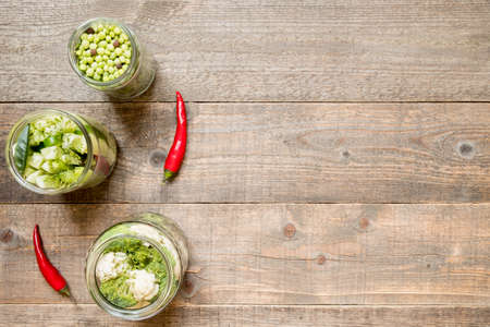 Top view jars with canned green vegetables and chilli on a wooden kitchen table. Preservation and preservation food concept. copy spaceの写真素材