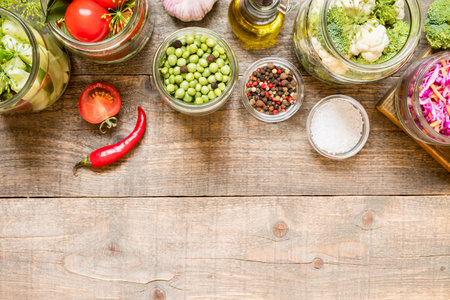 Top view jars with canned vegetables, raw ingredient and seasonings on wooden kitchen table. Food preservation and conservation conceptの写真素材