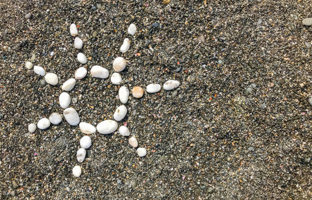 Sun of white pebbles on dark sand by the sea copy space.