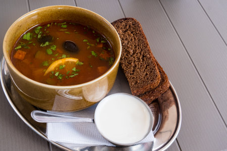 Traditional Russian meat soup solyanka in a bowl, with sour cream and black bread. Krasnaya Polyana,...