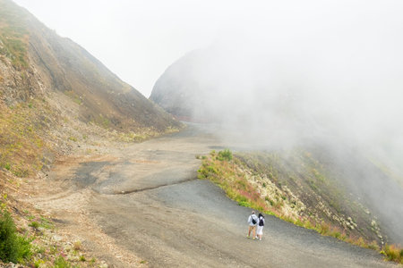 Couple with backpacks walks along the road against the background of a mountain landscape with...