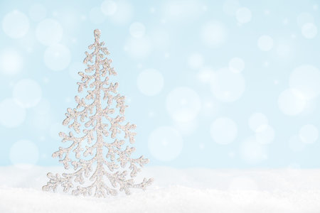 Christmas tree on surface with snow and defocused lights with copy space.