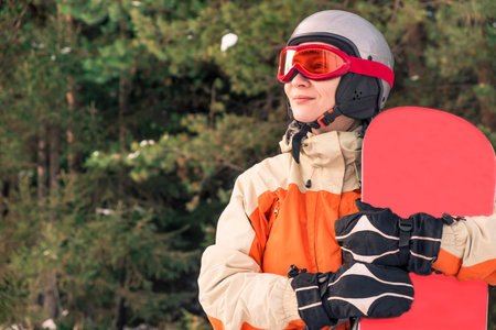 Portrait of a woman snowboarder in helmet and goggles in front of the forest.の写真素材