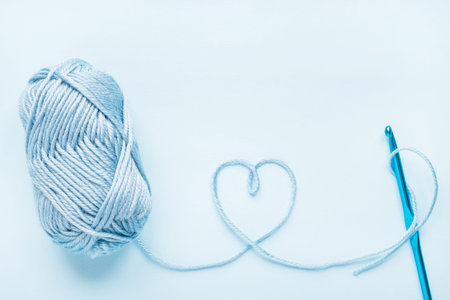 Crochet heart, hook and ball of yarn on a blue background with copy spaceの写真素材