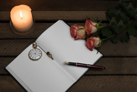 A notebook with a pen, clock, burning candle and 3 roses on a dark wooden backgroundの写真素材