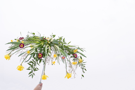 A hand holding an umbrella made of colorful spring flowers, daffodils, primeroses and greeneryの写真素材