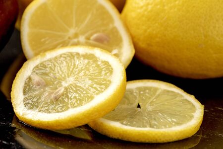 Frexh yellow lemons whole and slices on dark background with reflectionの写真素材