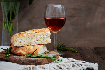 Sour dough focaccia flat bread with rosemary and salt on wooden cutting board and a glas of rose...