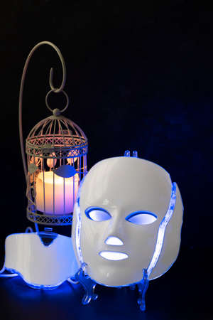 White plastic color therapy mask glowing blue with cage canle holde and candleの写真素材
