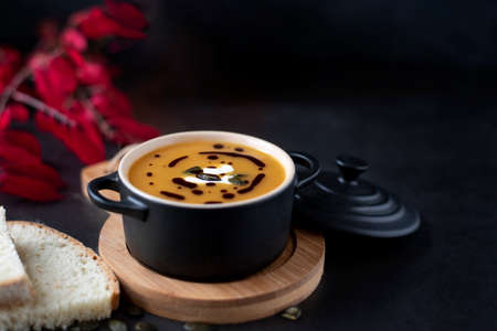 A bowl with orange pumpkin soup on wood with orange pumpkin and red leabes on black background, copy spaceの写真素材