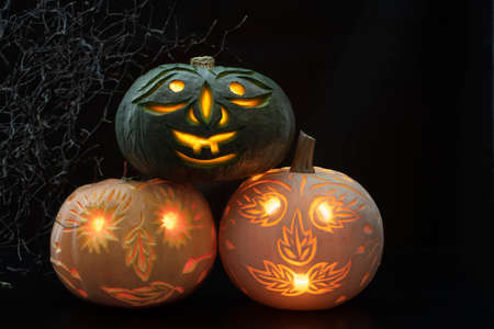 Green pumpkin, standing on orange and white pumpkins, all three carved on dark backgroundの写真素材