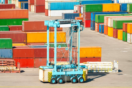 Container handler vehicle in cargo terminal with stacked multicolored cargo containersの写真素材