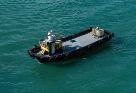Small industrial tugboat or utility vessel with a yellow cabin, floating on turquoise water