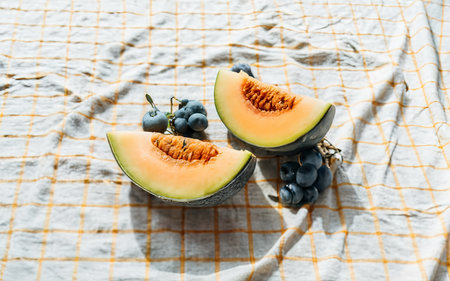 Cut yellow melon, grapes on the tableclothの素材