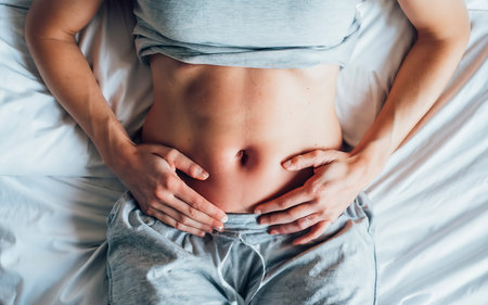 Healthy nutrition and belly health concept. Close up of woman flat stomach. Girl in bed with hungry feeling. Top viewの素材
