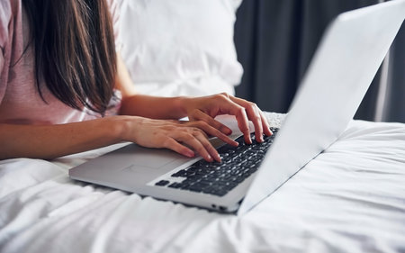 Close-up partial view of young woman using laptop on bedの素材
