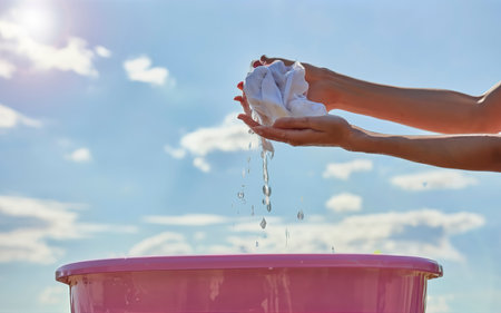 Female Hand washing clothes in the pink basin with clear Bubble soap against blue sky and sunlight.の素材