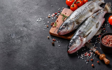 Fresh raw seabass with spices and tomatoes on a branch. On black rustic backgroundの素材