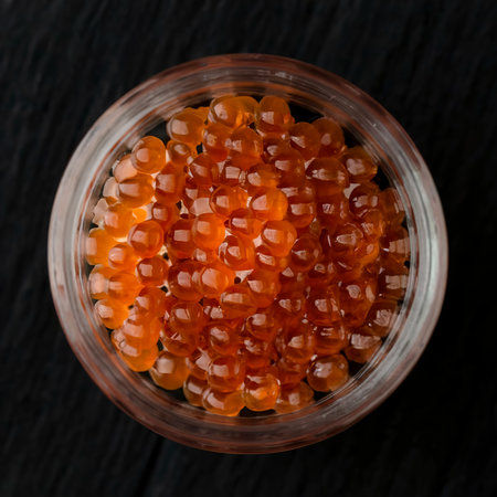 Red caviar in a glass jar on a black background. Close-upの素材