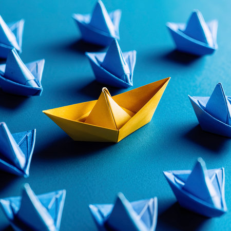 Set of origami boats. One Yellow paper boat leading among Blue ships on blue backgroundの素材