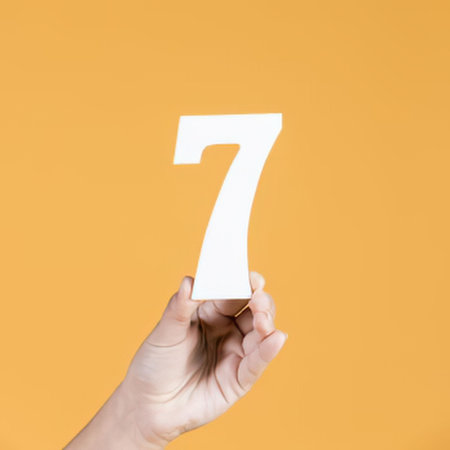 a fair-skinned hand holding a large white number seven against an orange background