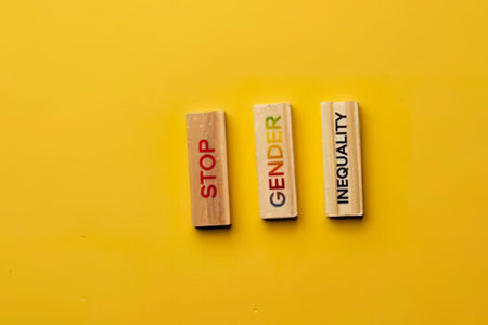 Three wooden blocks with words stop gender inequality on a bright yellow background